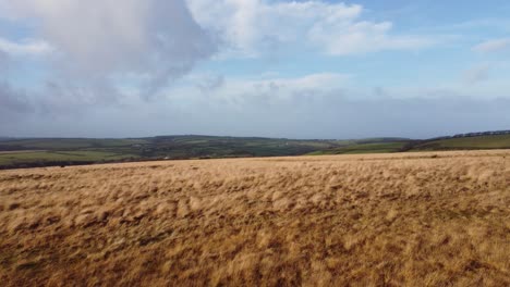 Aerial-View-Over-Moorland-with-Rolling-Fields-in-Background-and-Cloudy-Blue-Sky-UK-4K