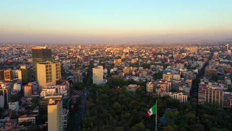 vibrant orange sunset over mexico city, parque hundido, aerial pull back mexican flag waving