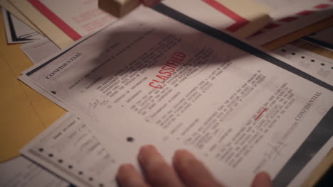 hand stamping secret paper document with ink stamp of classified text. label of security level clearance. marking of confidential folders and files on desk. military agent or government office analyst