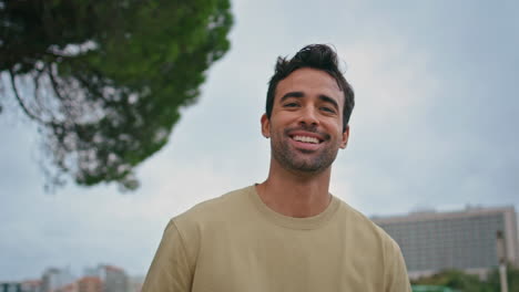 portrait smiling man urban park. happy hispanic guy posing at tree greenery