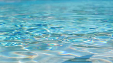 crystal clear blue pool water shimmers and shines with reflections on surface and bokeh lights in background, static close up