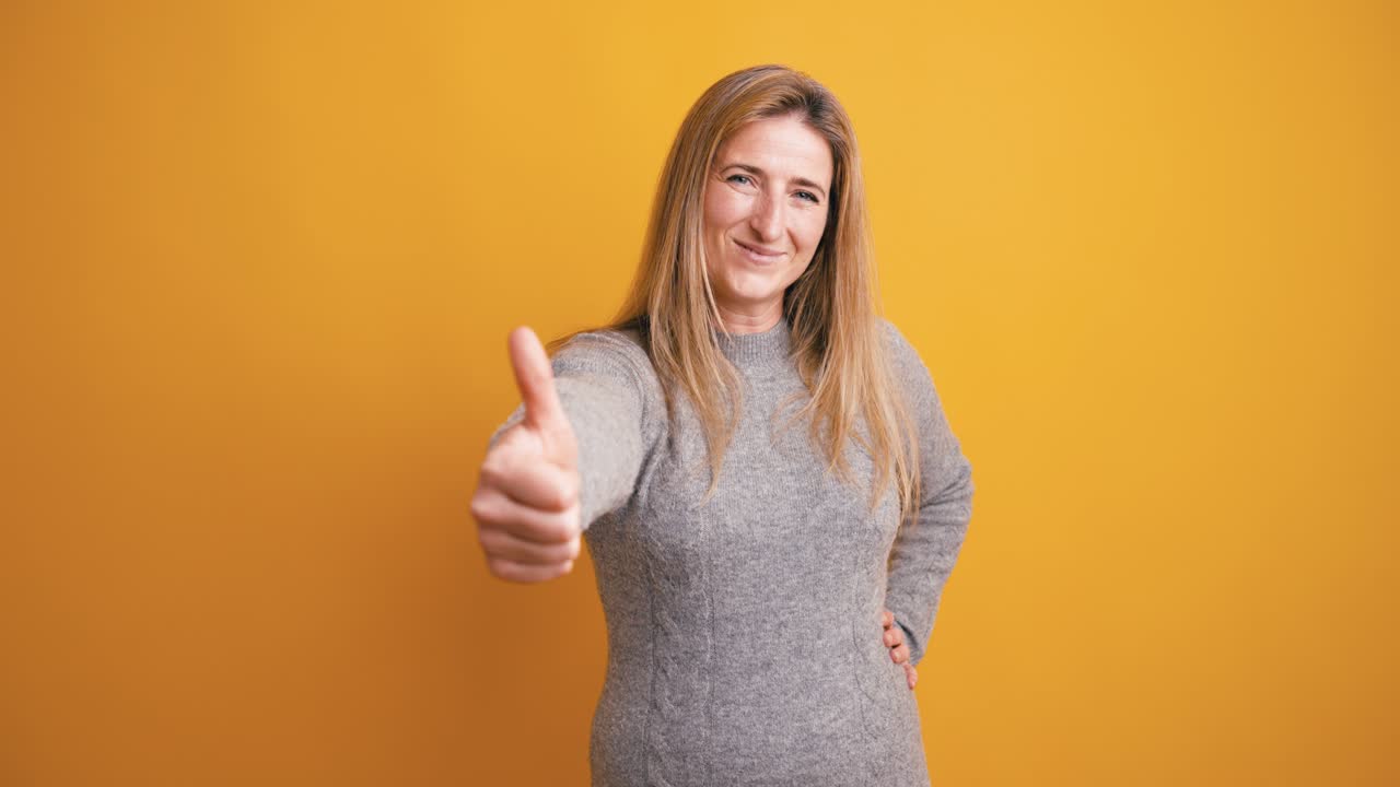 Donna felice che fa il gesto del pollice in su su sfondo giallo.