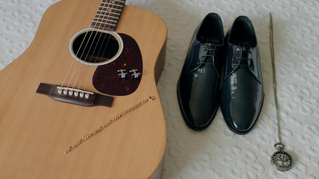 Guitar, pudsede sorte sko, en guldkæde og et antikt lommeur lagt ud på et hvidt sengetæppe