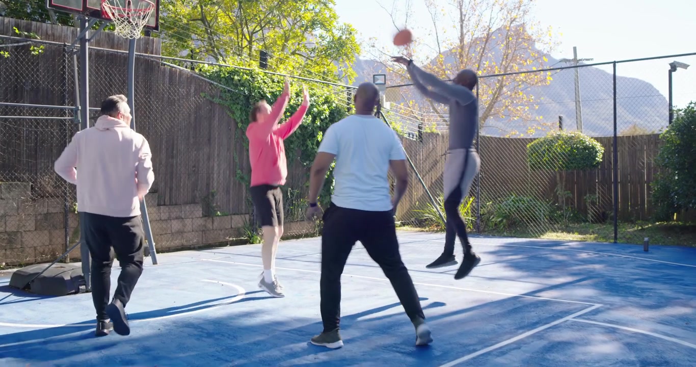 Afro-Amerikaanse man met roze hoodie maakt fopbeweging, dribbelt op omheind veld met basketbal, probeert te scoren