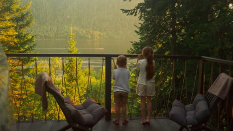 children admire view of lake with water transport and surrounding mountains. family recreation in country hotel for tourists with glamping complex in autumn