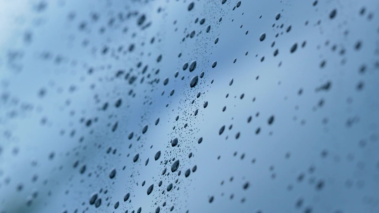 Close up macro shot of water droplets on a window pane during a storm, featuring a soft blue bokeh background. Ideal for wellness and nature themes.