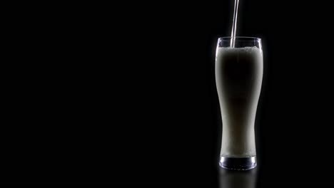 a glass of beer is poured on a black background