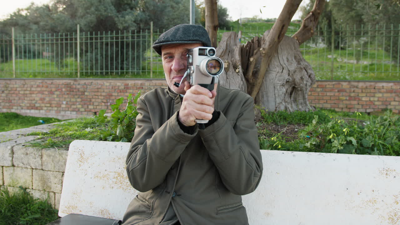 Man Sitting on a Park Bench While Filming with His Vintage Camera