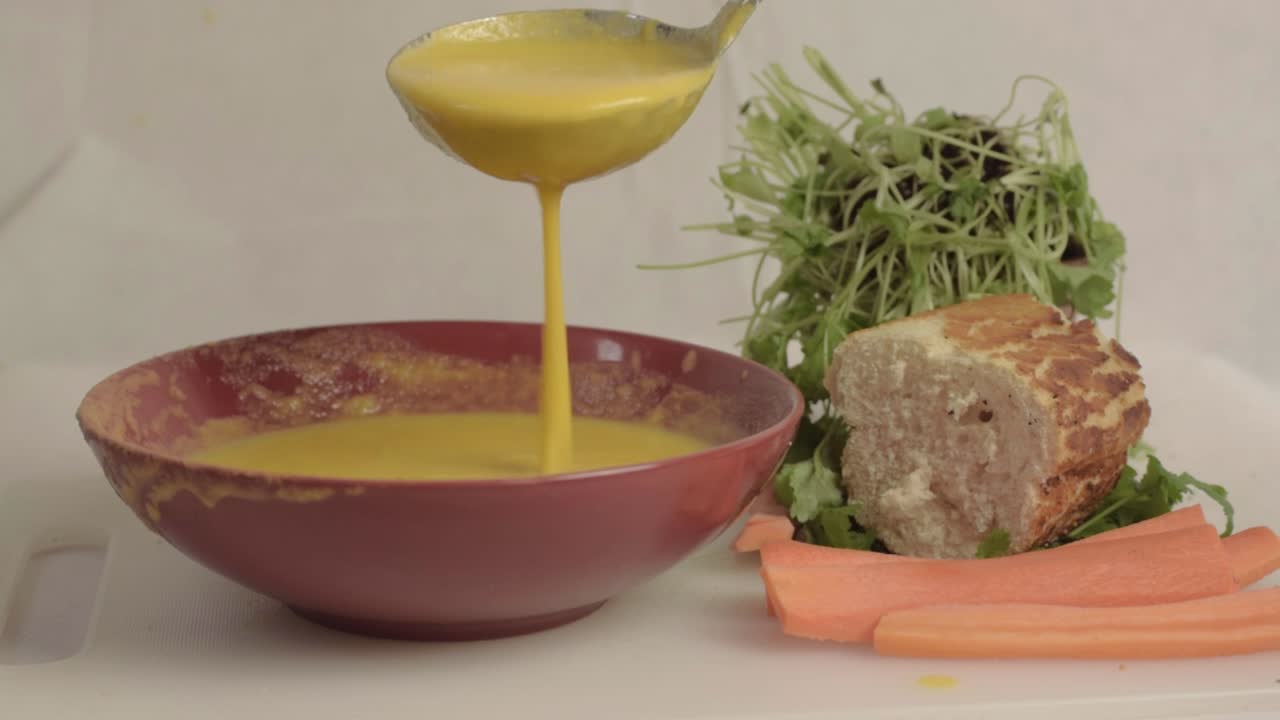 Pouring fresh carrot and coriander soup into a bowl with a ladle medium shot