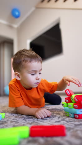 adorable caucasian toddler lies on the floor playing with toys. tower falls apart and kid smiles. vertical video.