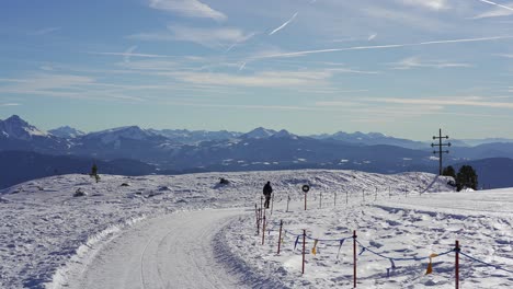 Hiker-walks-alone-along-a-snow-path-on-the-peak-of-a-deserted-snow-capped-mountain-with-epic-mountain-peaks-in-the-background