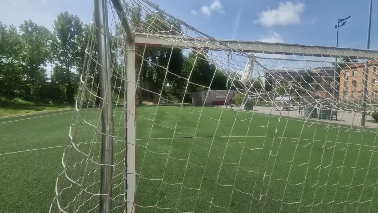 Point of view shot showing an empty soccer goal and green artificial turf on a sunny day