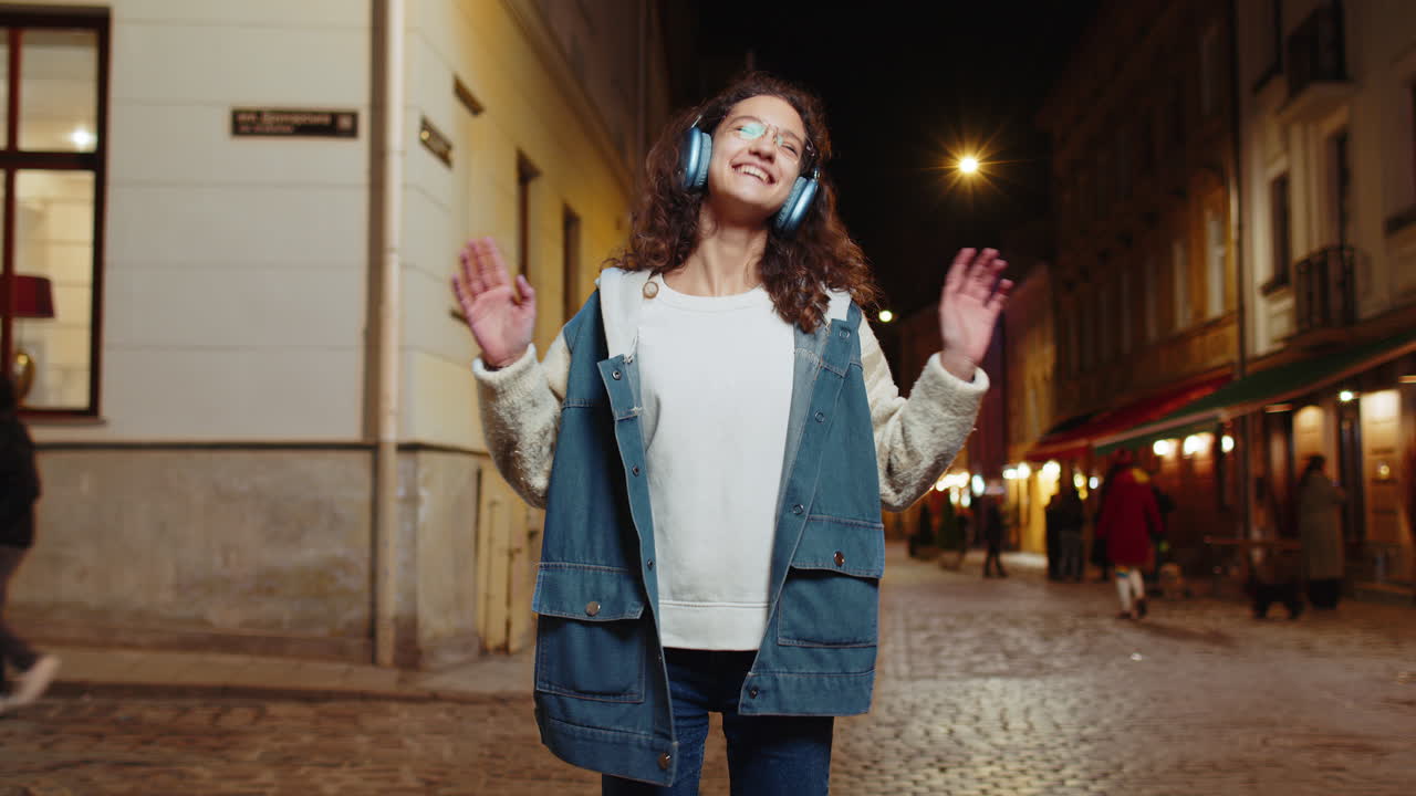 Happy teenager child girl kid in wireless headphones listening music dancing in night city street