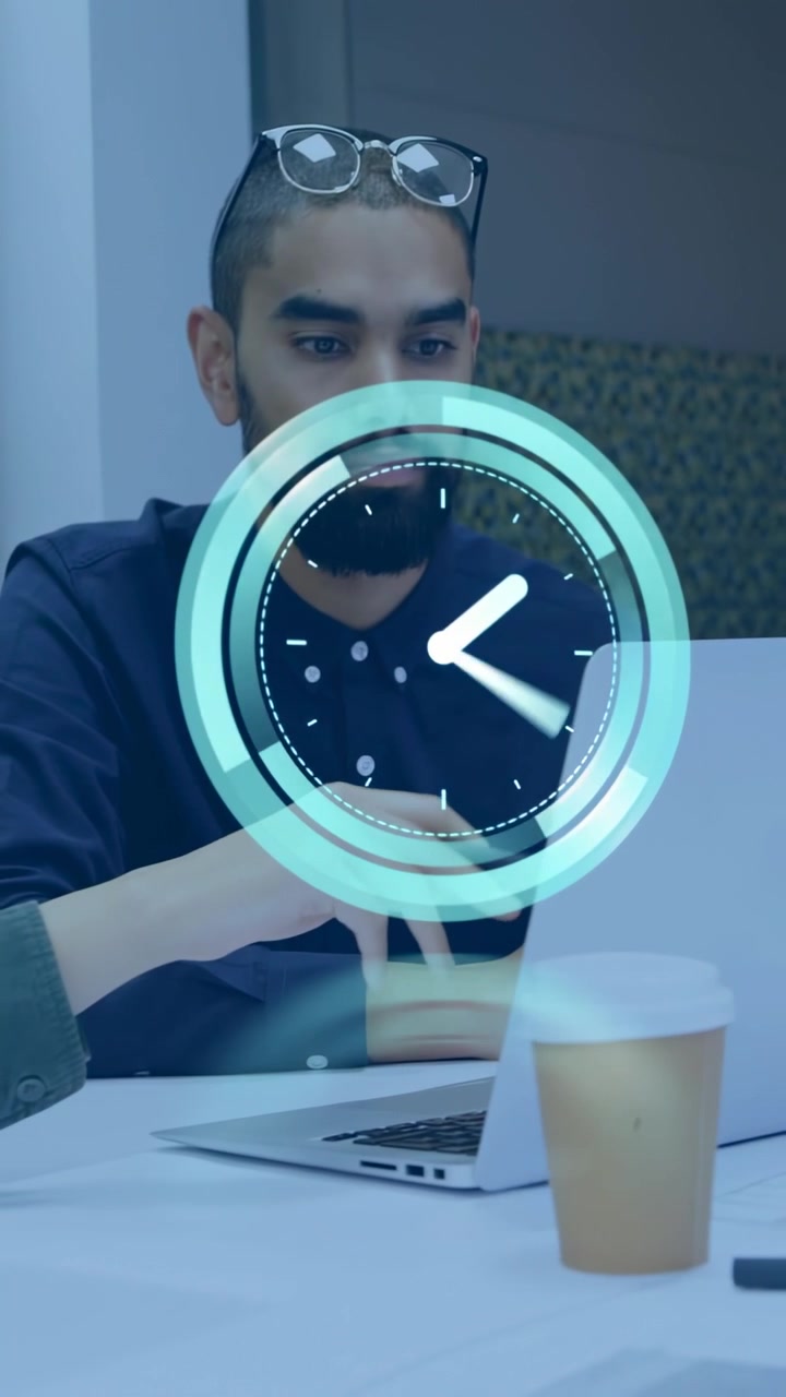 Hombre adulto trabajando en la oficina, con camisa oscura, portátil, taza de café, gafas, su antebrazo visible y un gráfico de reloj.