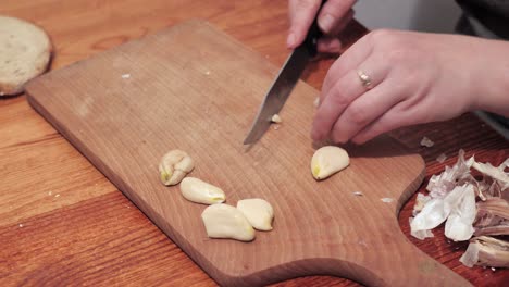 woman's hands with a knife crush the last clove of garlic on a chopping board, then peel the skin