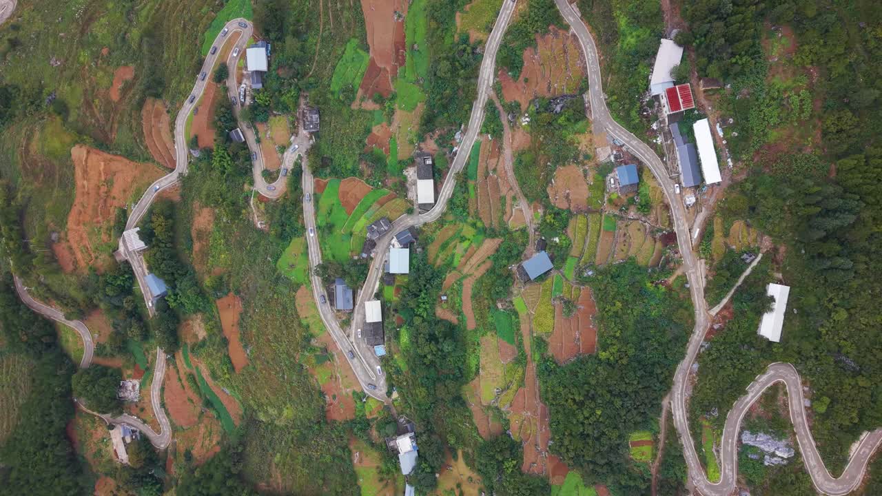 Aerial top-down view of winding serpentine roads cutting through the hills of Wuxi County, Lingpaishi, revealing zigzag paths, scattered homes, farmland patches and lush mountainous terrain. UHD