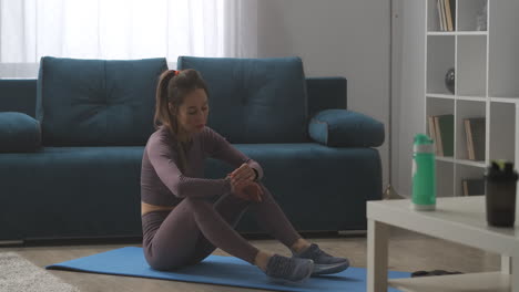 slender sporty woman is sitting on floor looking at fitness tracker gadget for healthy lifestyle home training and wellness concept