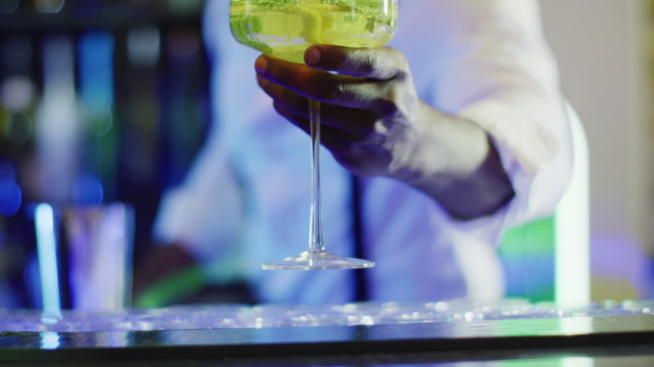 Video of midsection of african american barman serving green cocktail over the bar