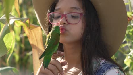 little girl playing and kissing a green parakeet