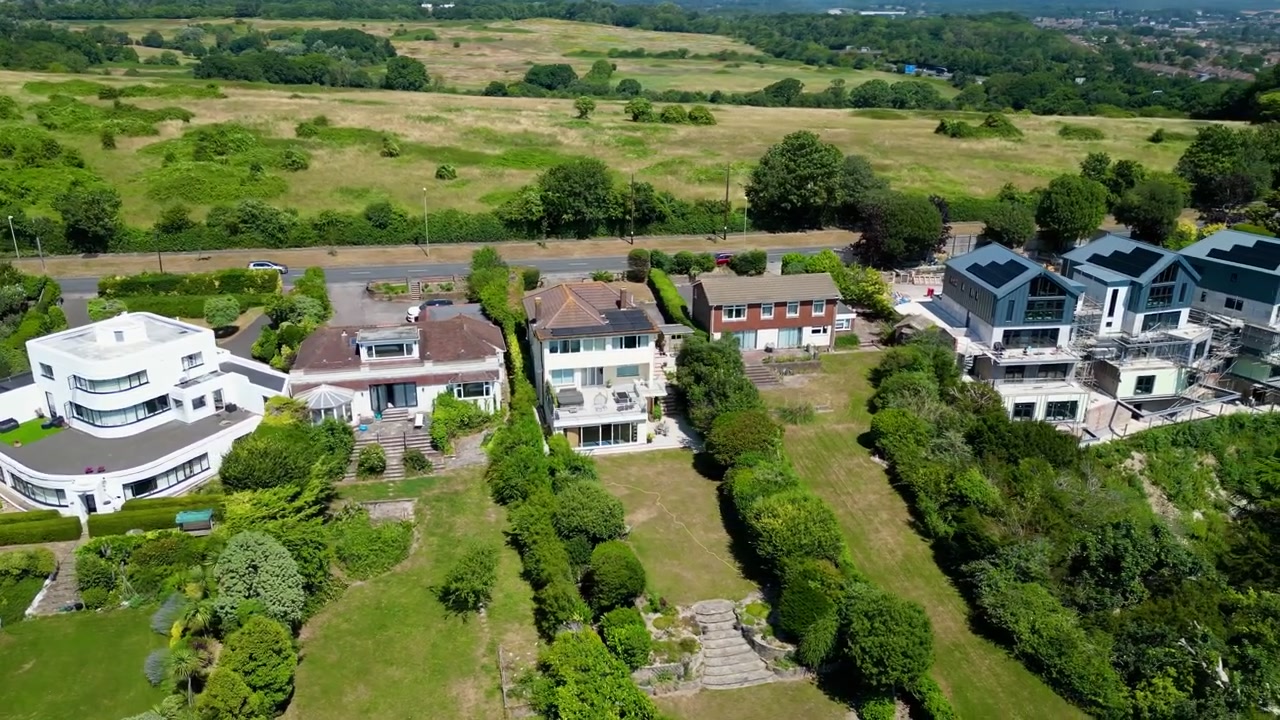 Prise de vue aérienne par drone de maisons de banlieue bordant Portsdown Hill, comprenant des maisons individuelles, des jardins résidentiels, des prairies ouvertes, des arbres et la campagne environnante près de Portsmouth.