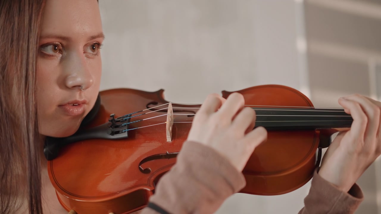Teen girl concentrates during violin warmup session. Closeup of girl tuning her violin in cozy sunlit room. Young female musician practicing her violin with focus and gentle bowing in welcoming space