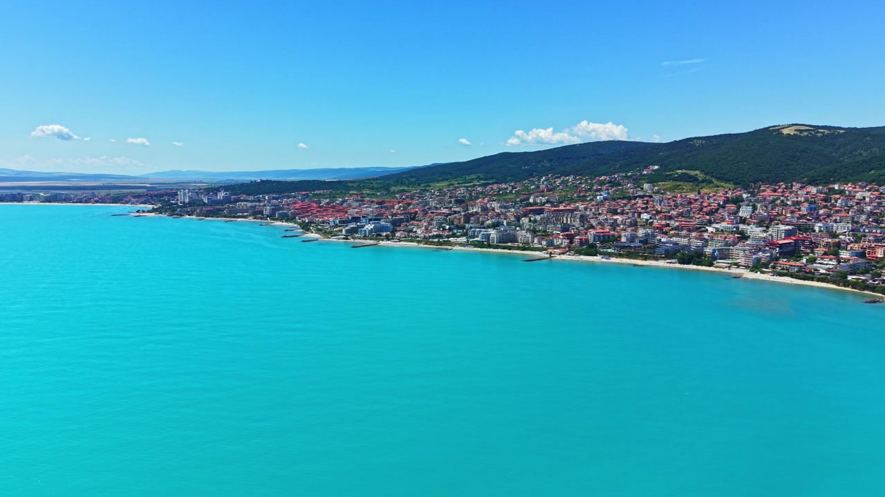 Yazın Sahil Şeridi, Berrak Su ve Arka Planda Kasaba Gösteren Plaj Manzarası, Mavi Gökyüzü Altında
