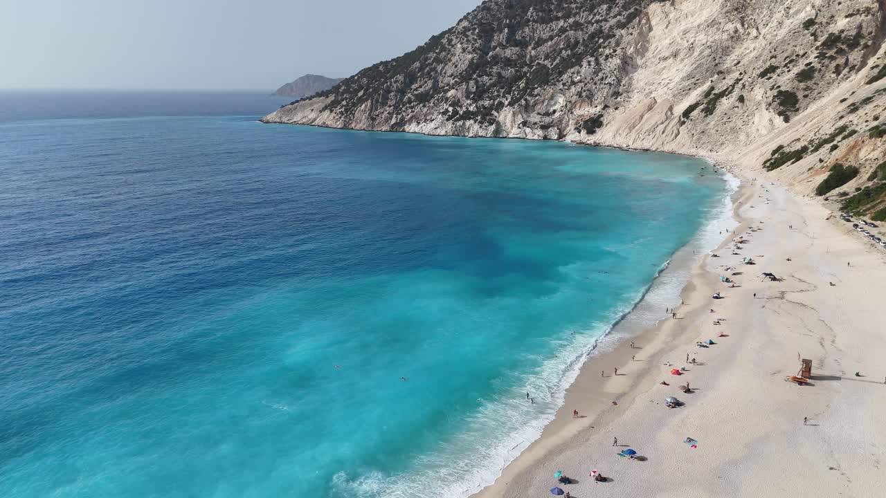 Pebble stone white beach with turquoise water on a sunny day with big waves.