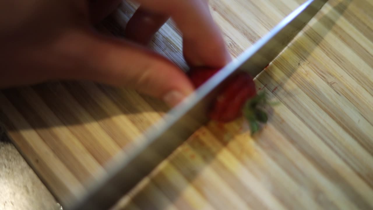 toma en cámara lenta de alguien que usa un cuchillo afilado para cortar algunas fresas rojas y frescas