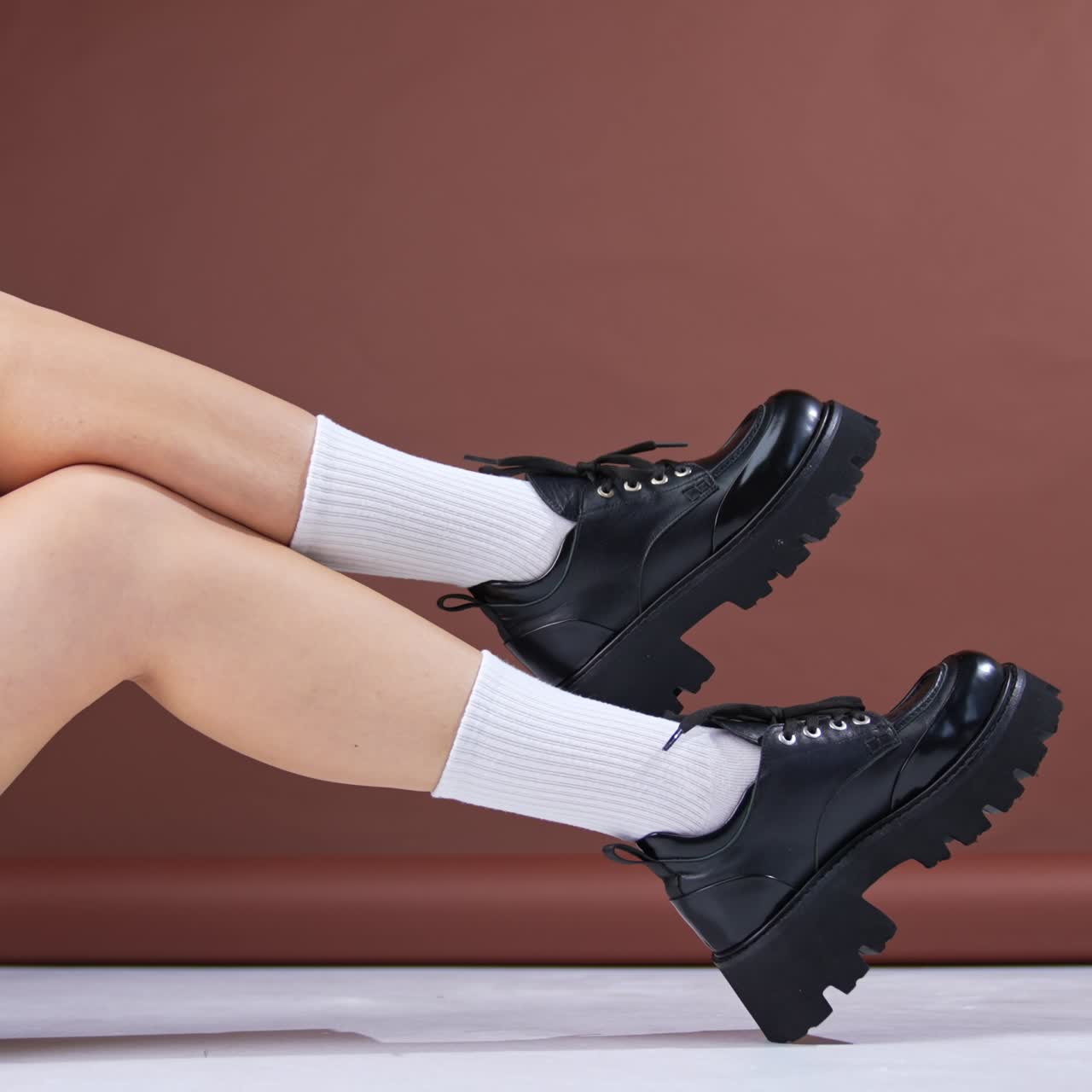 Girl lies on the floor wearing white socks and black modern shoes with laces. Woman in black bicycle shorts waves her legs showing the footwear