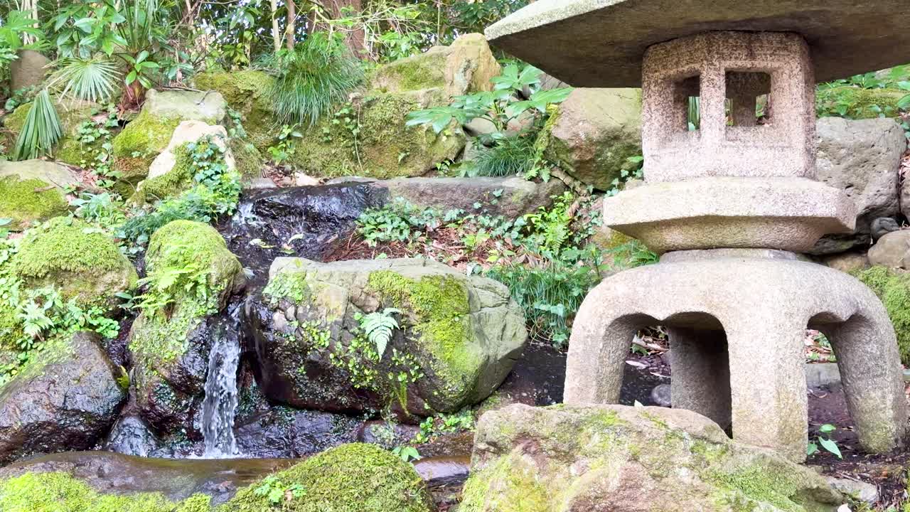 滝と苔むした岩の傍らにある石の灯籠を捉えた静止画の中距離ショット。