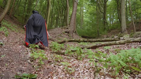 Mann-Mit-Schwarzem-Umhang-Und-Sense,-Der-Mit-Einer-Maske-Und-Einem-Tierschädel-Im-Wald-Spazieren-Geht