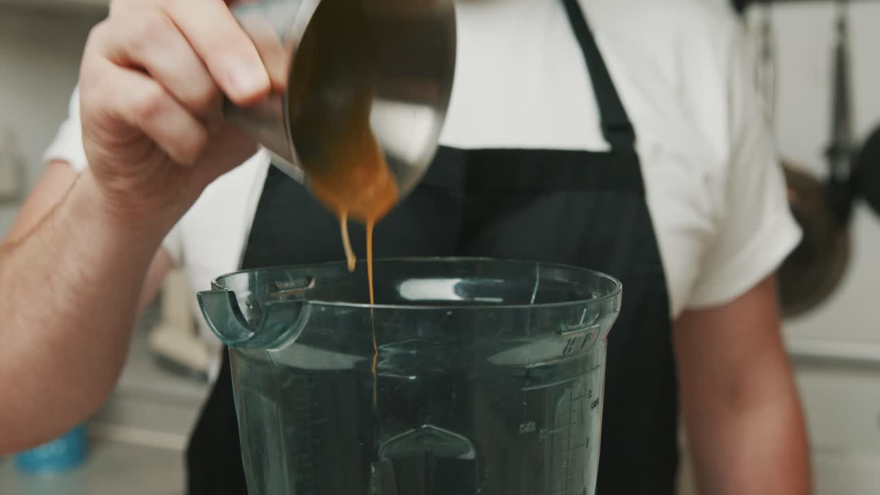 Uno chef con un grembiule nero e una maglietta bianca aggiunge quattro tuorli d'uovo in un frullatore