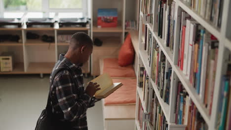 student chooses necessary literature for individual task. black man reader learns literature for personal investigation in university library. guy reads book