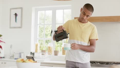 Hombre-Birracial-Feliz-Haciendo-Café-En-Una-Cocina-Luminosa,-Cámara-Lenta