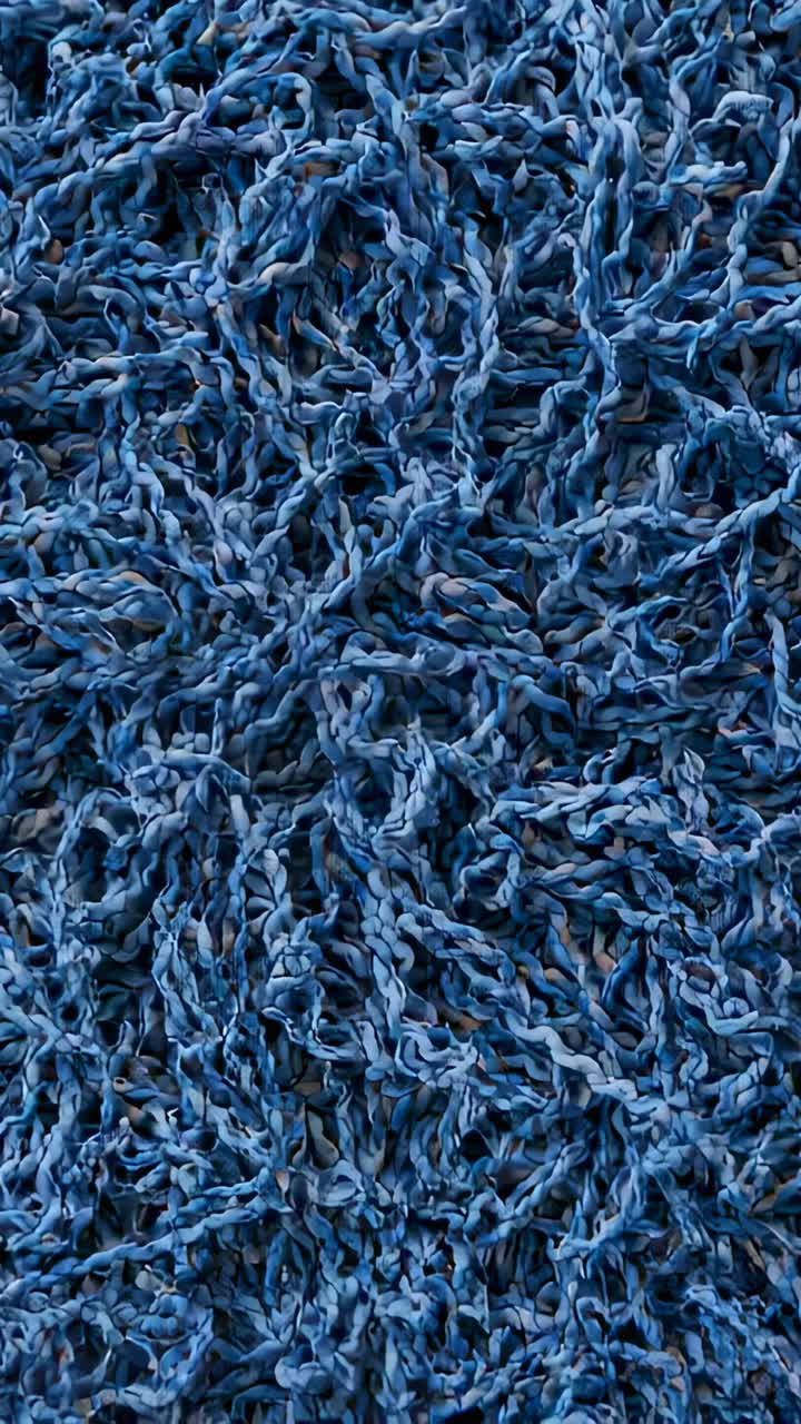 Vertical video: Shifting camera revealing dense blue looped textile closeup showing yarn texture