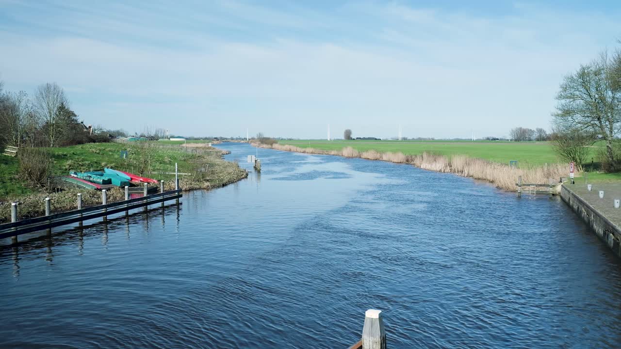 Bred kanal som flyter gjennom grønne jorder med vindturbiner i det fjerne