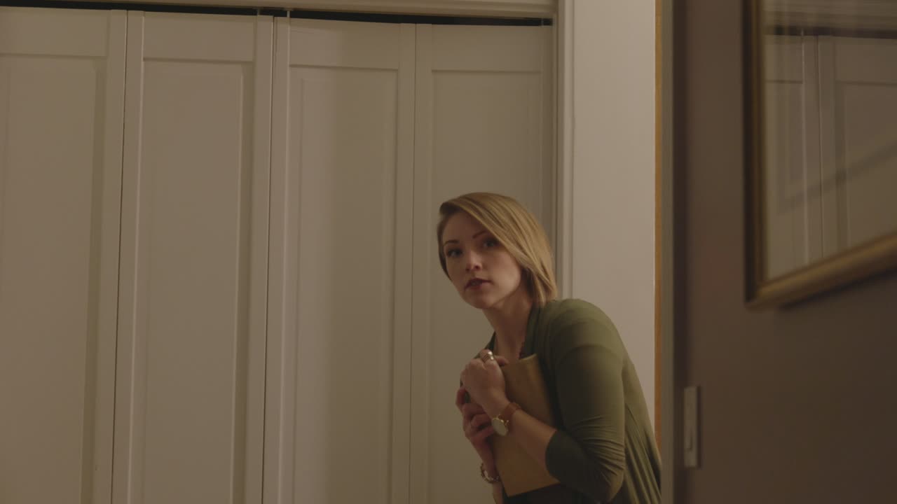A frightened woman is seen looking around a doorway to see if someone is there