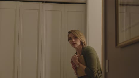 a frightened woman is seen looking around a doorway to see if someone is there