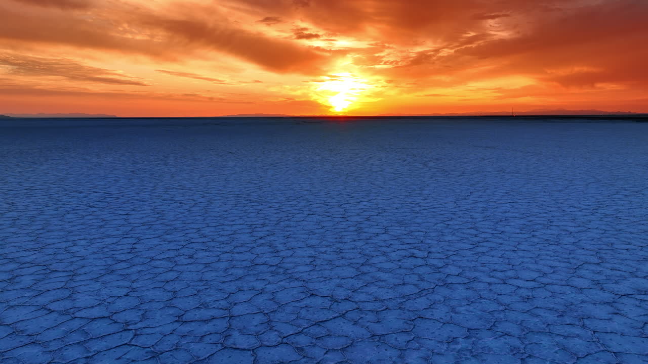 Volo sopra la terra blu screpolata nella distesa salata di Bonneville, Utah, USA. Splendido cielo arancione con nuvole sopra il paesaggio