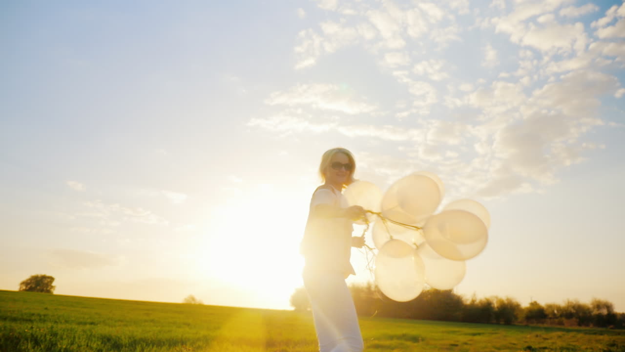 석양에 푸른 초원을 걷고 있는 풍선을 든 평온한 젊은 여성