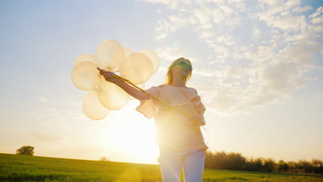 Mujer-Joven-Despreocupada-Con-Globos-Caminando-Sobre-Un-Prado-Verde-Al-Atardecer