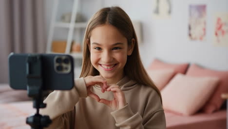 young girl vlogging and making a heart gesture with hands