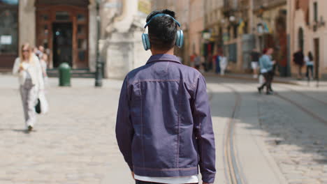 rear view of young man tourist walking through the street outdoors looking searching for a way