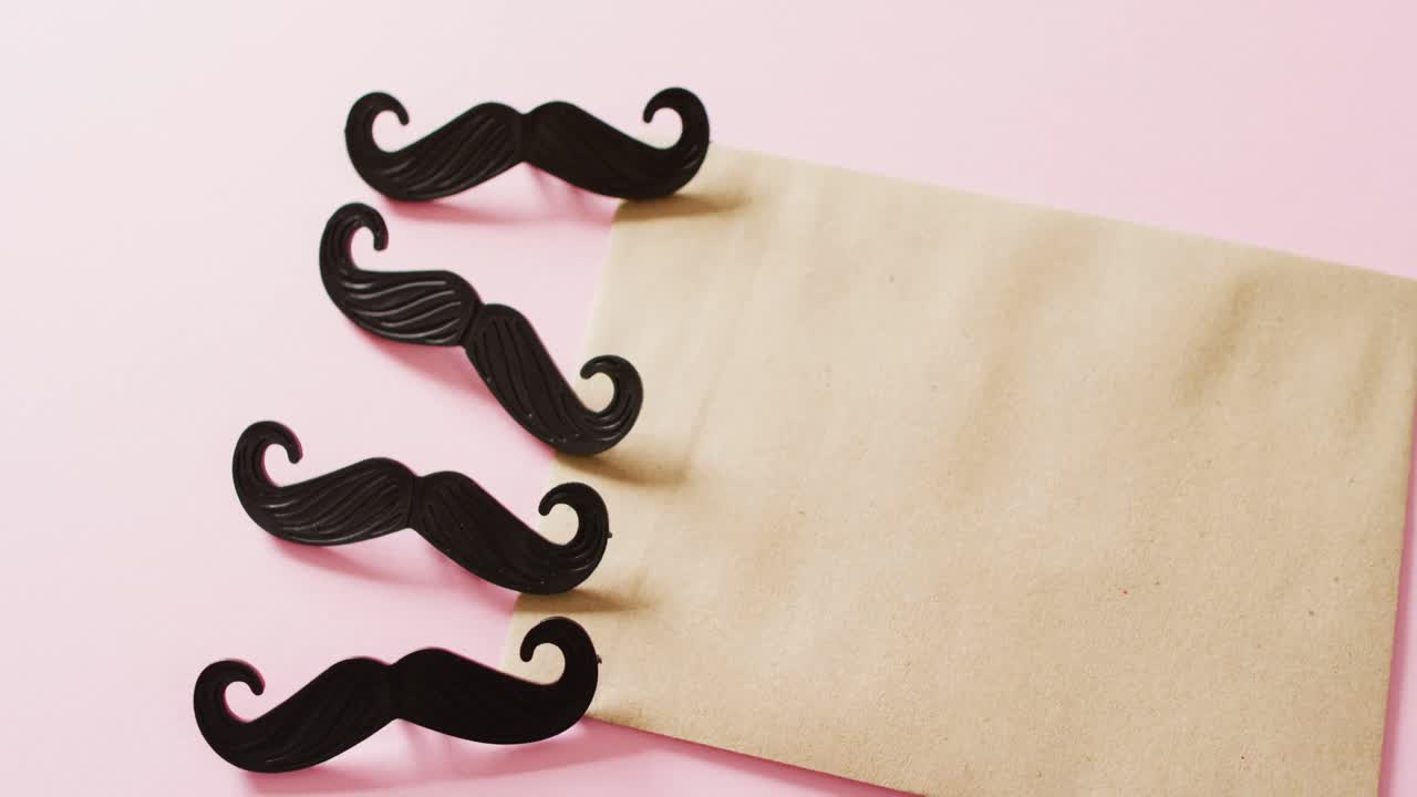 4개의 검은색 가짜  ⁇ 수염과 분홍색 배경에 복사 공간이 있는 노란색 봉투의 비디오