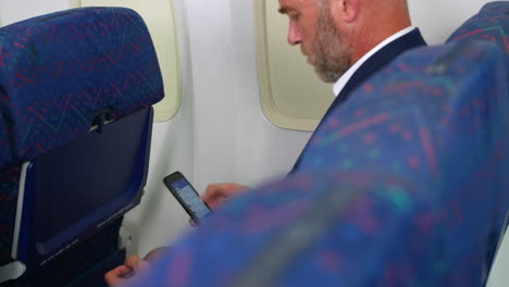 un hombre de negocios chequeando mensajes en el teléfono celular en un avión de pasajeros