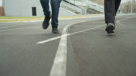 close up leg view of two people jogging on a track painted white in a stadium as they make a bend with with a white parked vehicle behind them