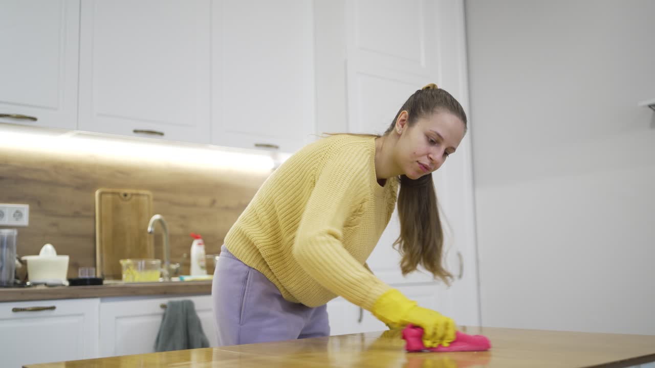 Mujer realizando la limpieza de primavera, usando un paño de microfibra en una mano mientras limpia otra zona con la otra, destacando el cuidado exhaustivo del hogar, la higiene y el mantenimiento doméstico en un entorno familiar.