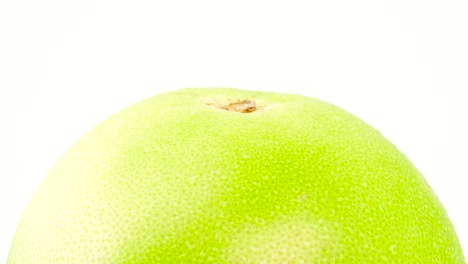 macro shooting of upper part of green oroblanco fruit with water drops. rotating. isolated on the white background. close-up.