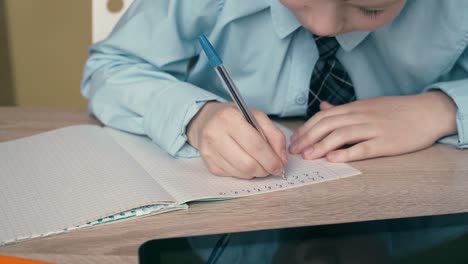 ext cu tracking schoolboy does homework writes a pen in a notebook on the table is a tablet