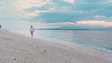 Beautiful-woman-walking-along-tropical-sandy-beach-during-golden-sunrise